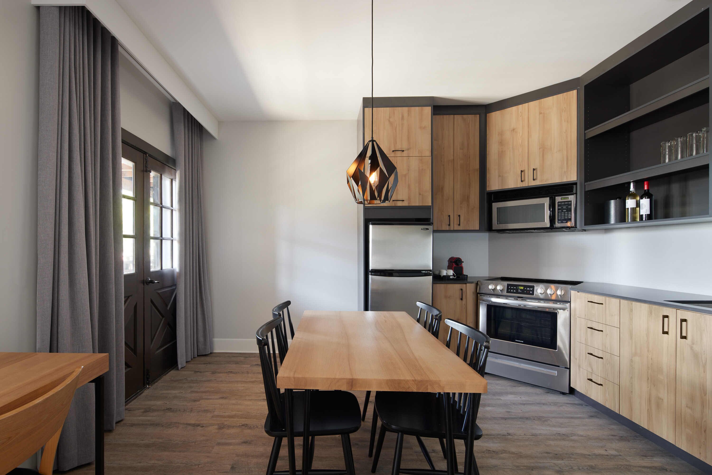 Una cocina moderna con una mesa de comedor de madera, sillas negras y electrodomésticos integrados.