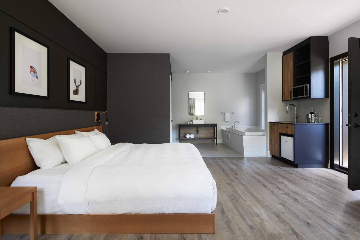A modern bedroom with a wooden bed, a small bedside table, a built-in desk, and a dark-colored wardrobe.