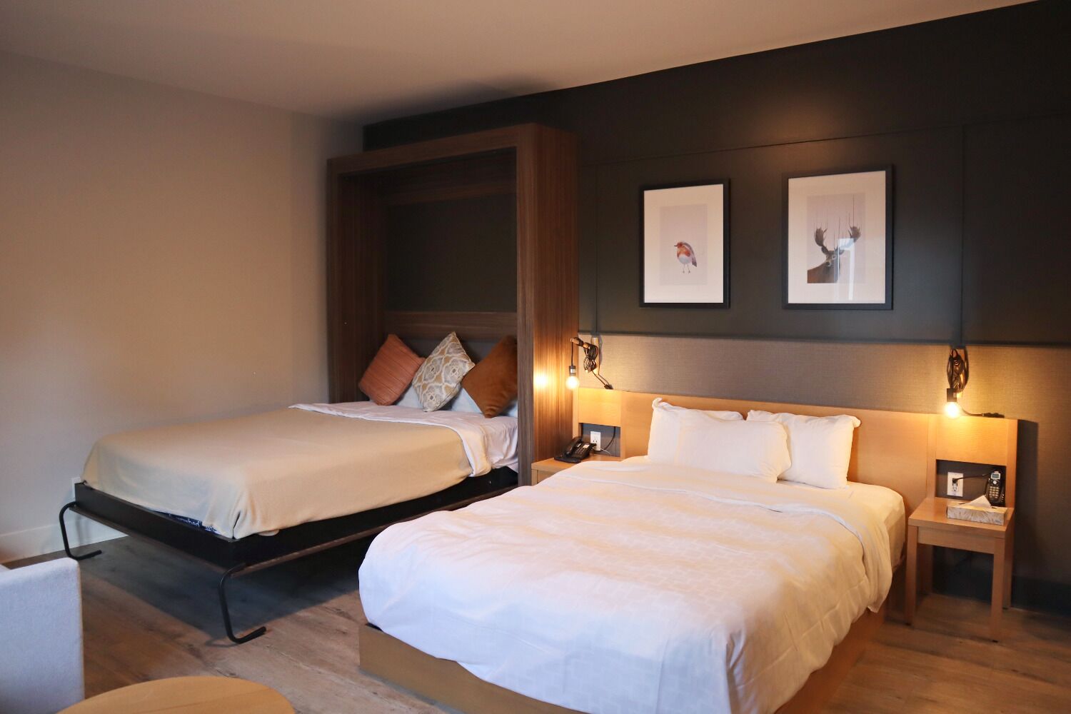 Habitación de hotel con dos camas, cabecero de madera, mesitas de noche con lámparas y cuadros en la pared.