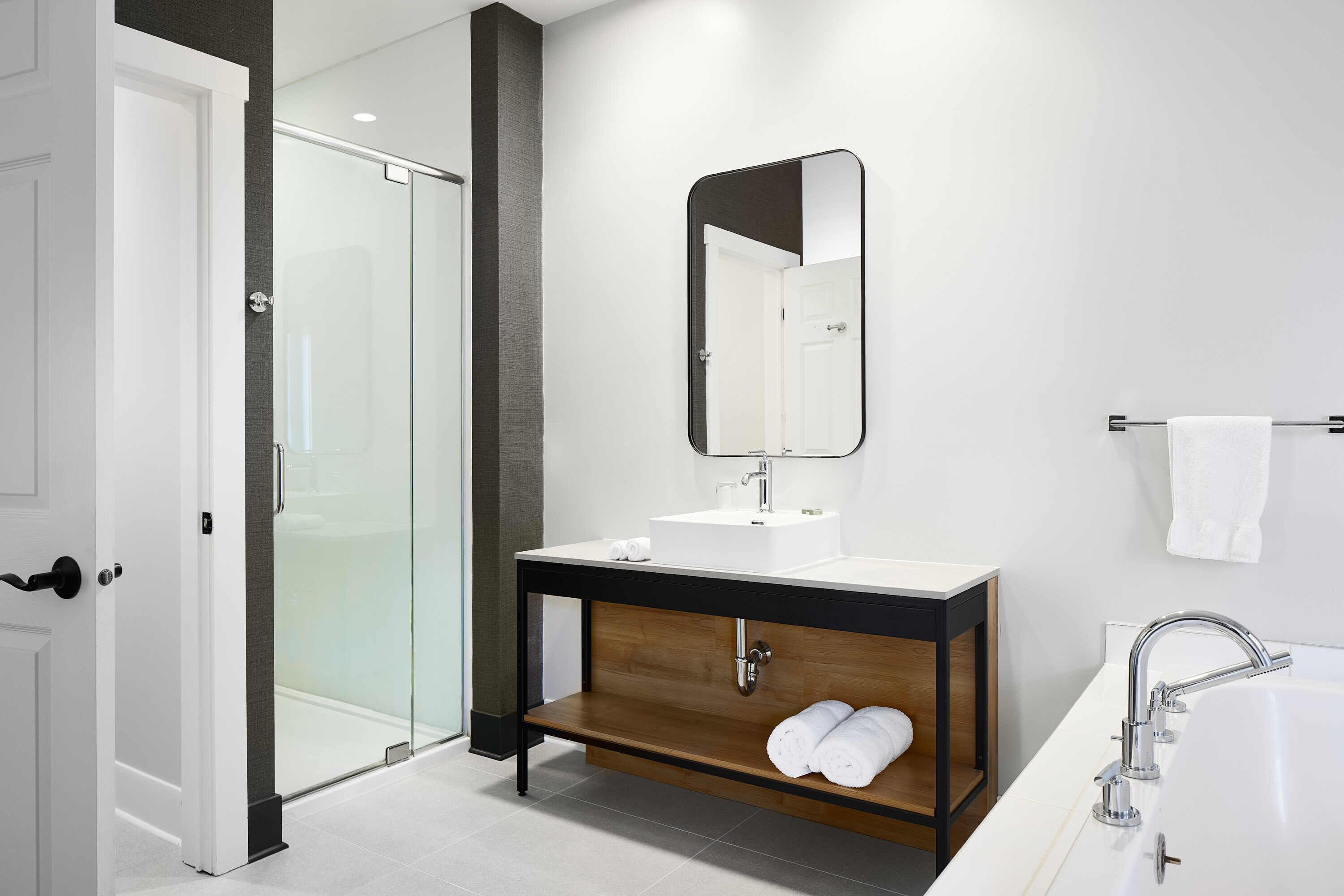 Une salle de bain moderne avec une douche à parois de verre, un meuble-lavabo en bois avec un miroir et un lavabo blanc.