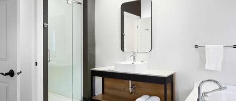 A modern bathroom with a glass shower enclosure, a wooden vanity with a mirror, and a white sink.
