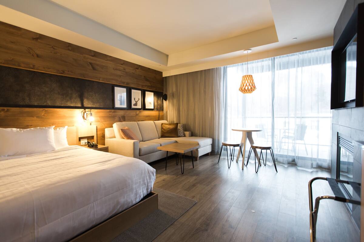 A modern hotel room with a large bed, a sofa, a small table, and a TV.