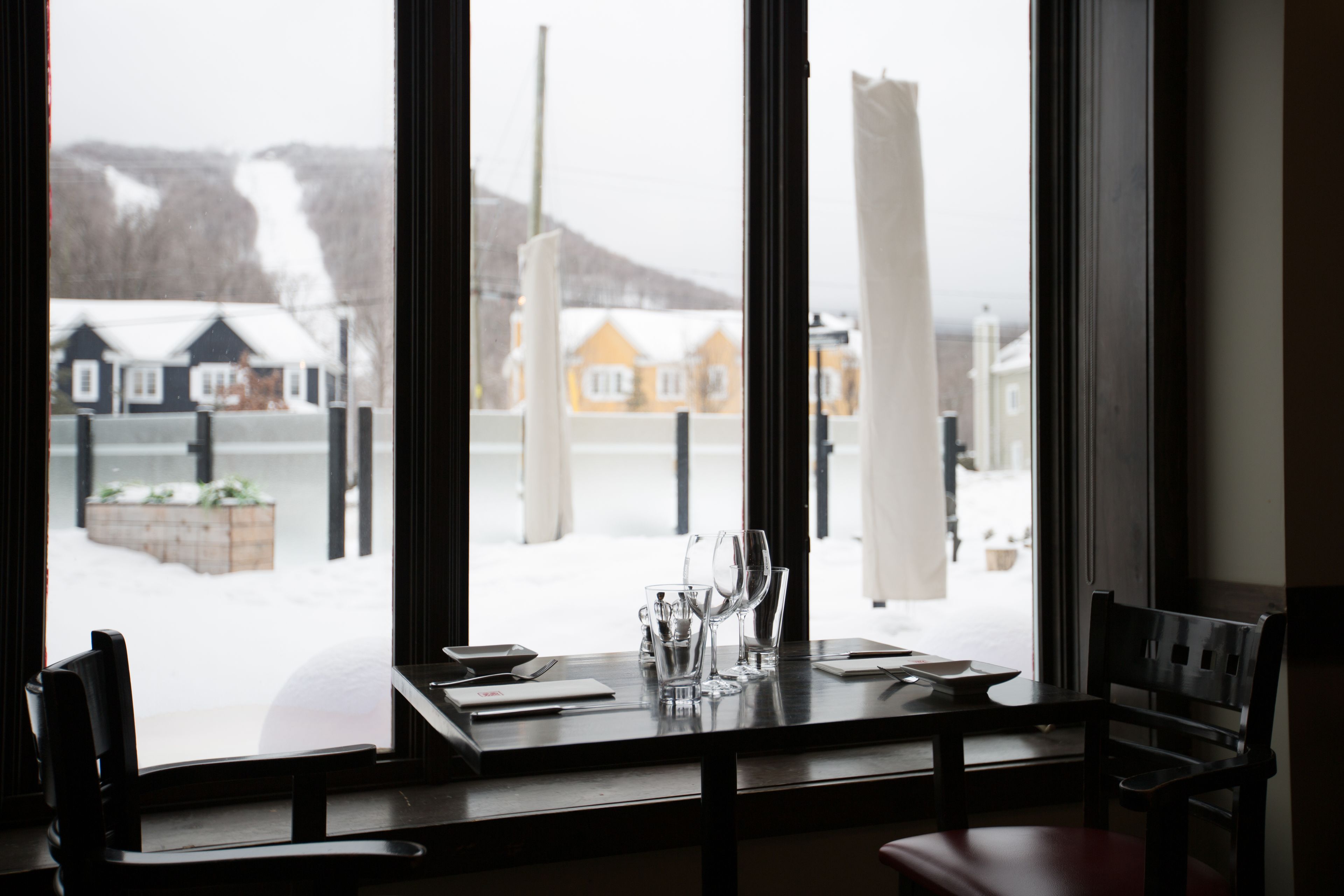 Ein Esstisch mit Stühlen, ein Fenster mit Blick auf Häuser und eine verschneite Landschaft.