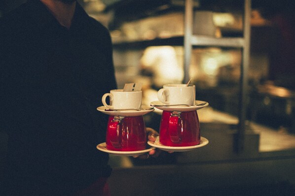 A person holding two teacups with saucers, one white and one red, on a tray.
