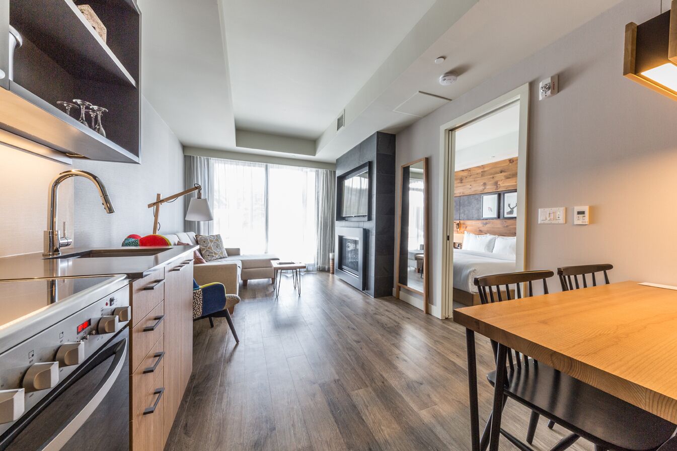 Eine moderne Küche mit Einbauofen, eine Essecke mit Holztisch und Stühlen, ein Sofa und ein großes Fenster, das für natürliches Licht sorgt.