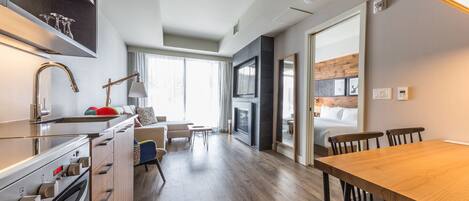 Eine moderne Küche mit Einbauofen, eine Essecke mit Holztisch und Stühlen, ein Sofa und ein großes Fenster, das für natürliches Licht sorgt.