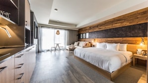 Een moderne hotelkamer met een groot bed, een houten accentmuur, een zithoek met een tafel en stoelen, en een keuken met een ingebouwde oven.