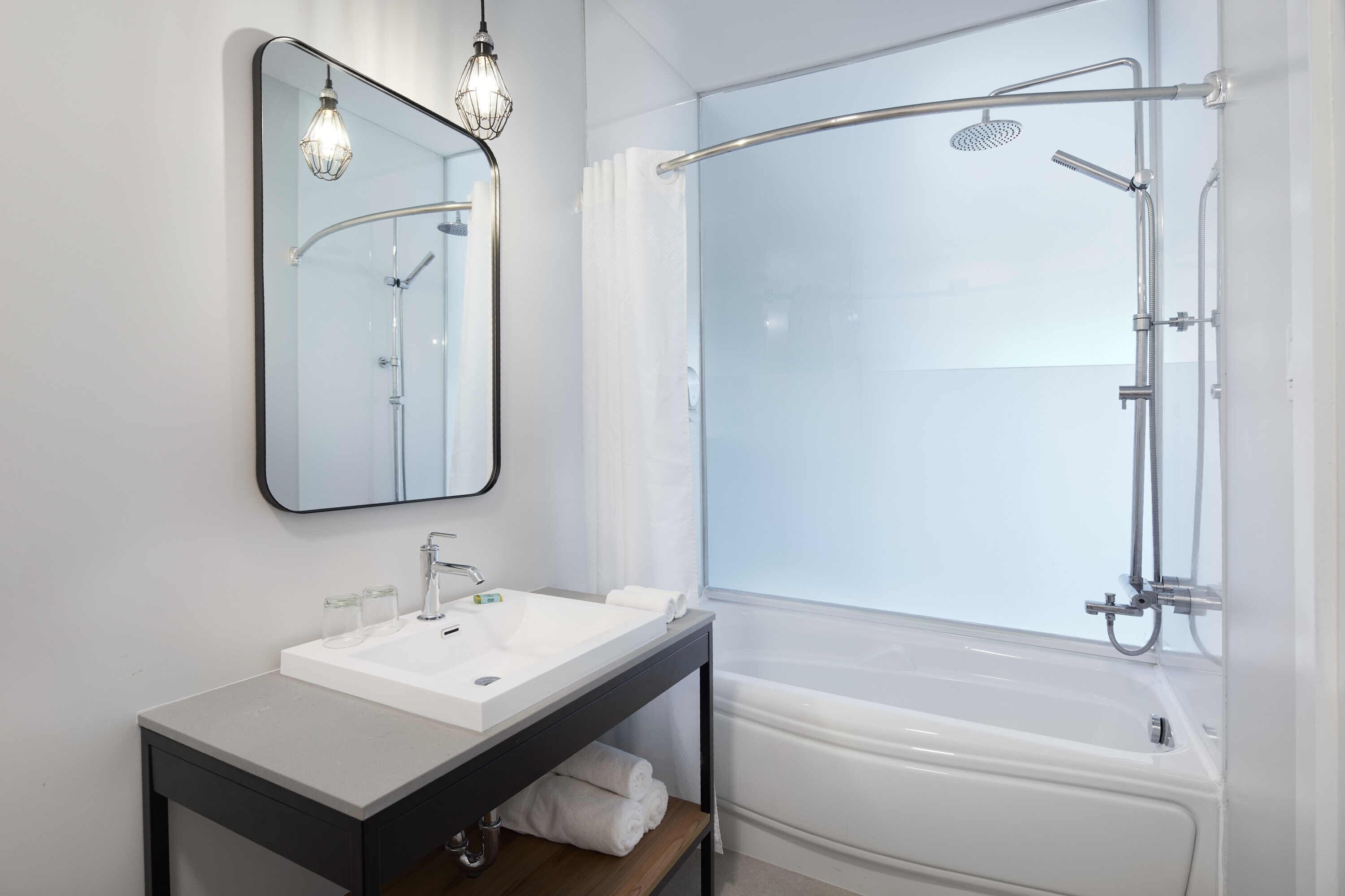 A modern bathroom with a white sink, mirror, and shower.