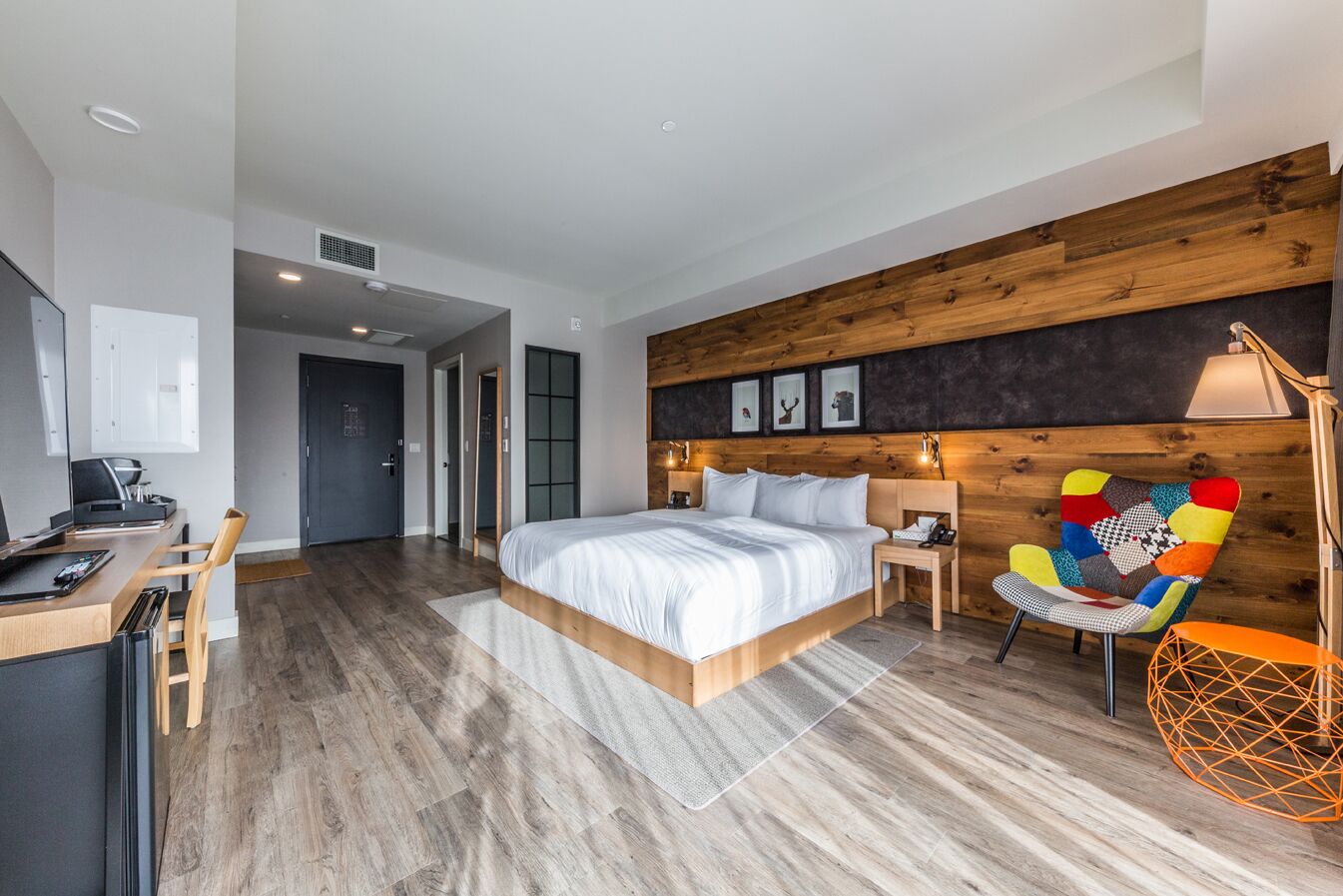 A modern bedroom with a large bed, a desk, and a colorful chair.