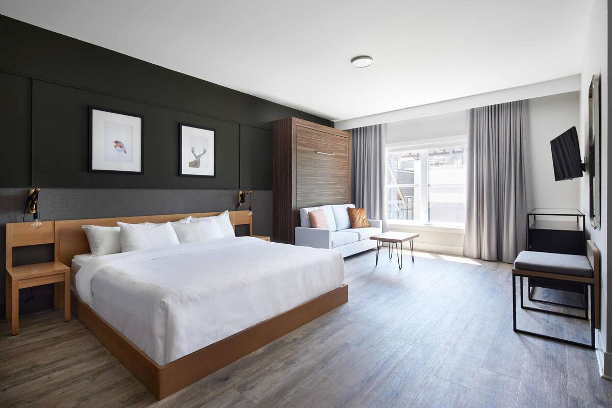 A modern hotel room with a large bed, a sofa, a small table, and a TV.