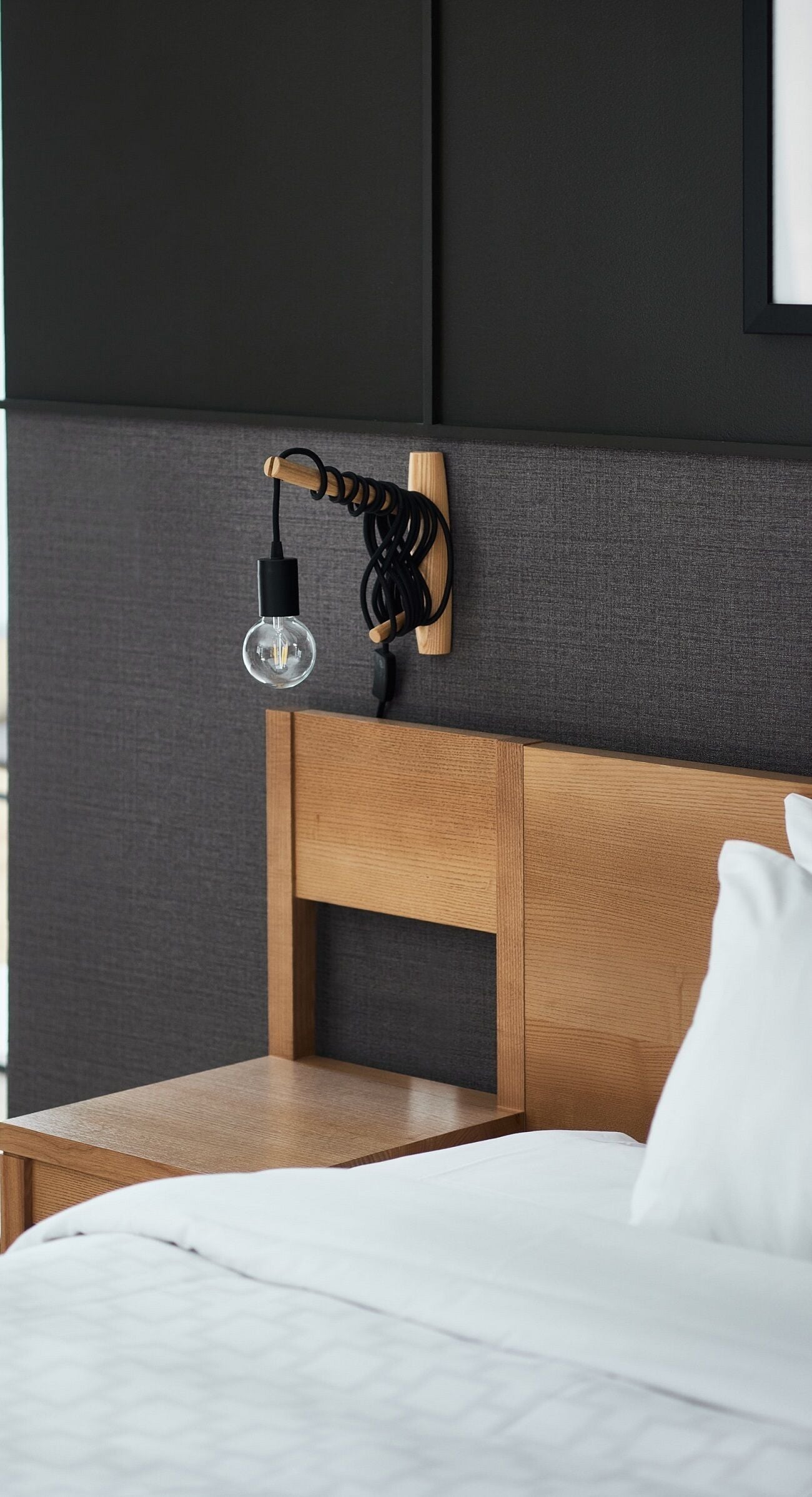 Un dormitorio moderno con cabecera de madera, mesita de noche y lámpara de pared.