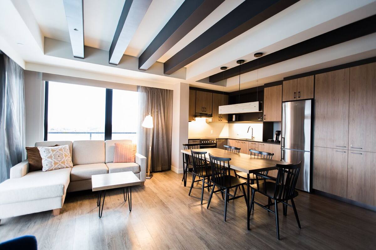 A modern kitchen with a dining area, wooden cabinets, and a large window providing natural light.
