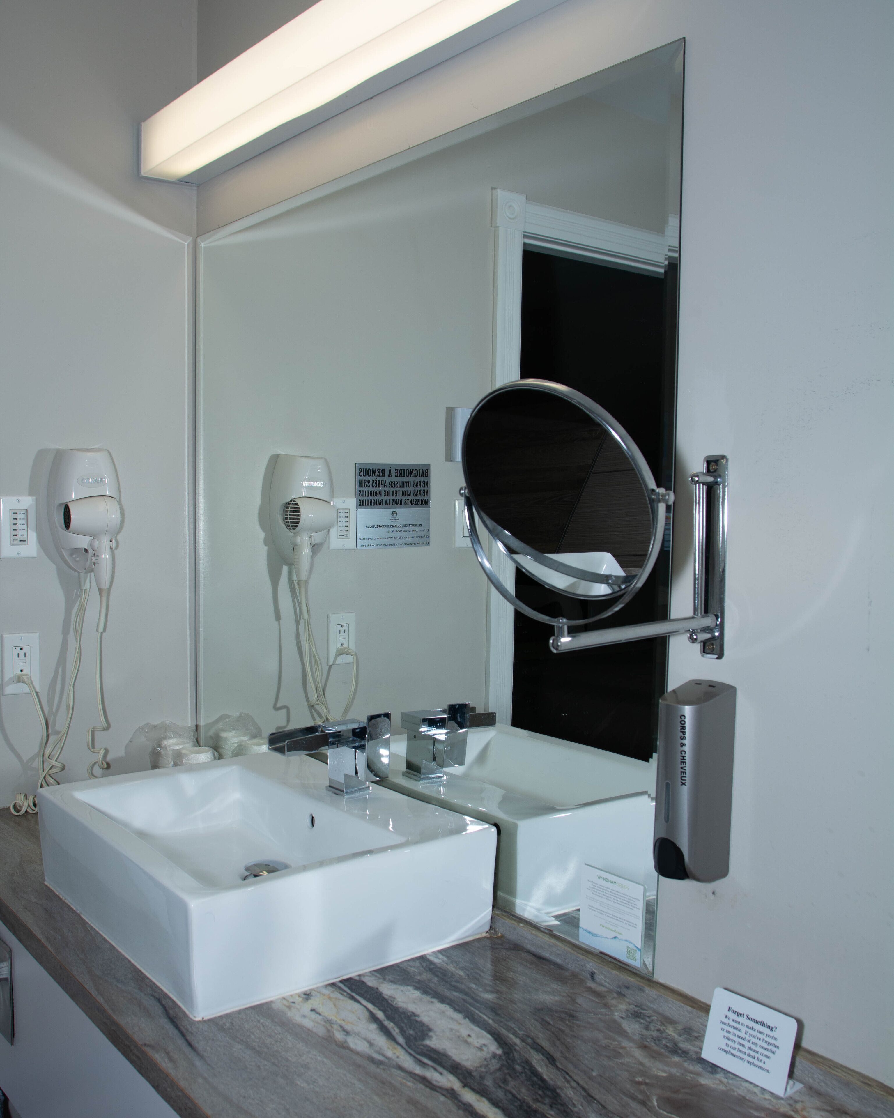 Un baño con dos lavamanos, un espejo grande y un secador de pelo en la pared.