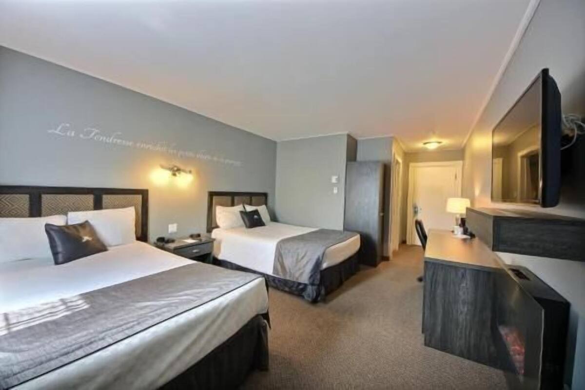 Ein Hotelzimmer mit zwei Betten, einem Schreibtisch, einem Stuhl, einem Fernseher und einem wandmontierten Spiegel.