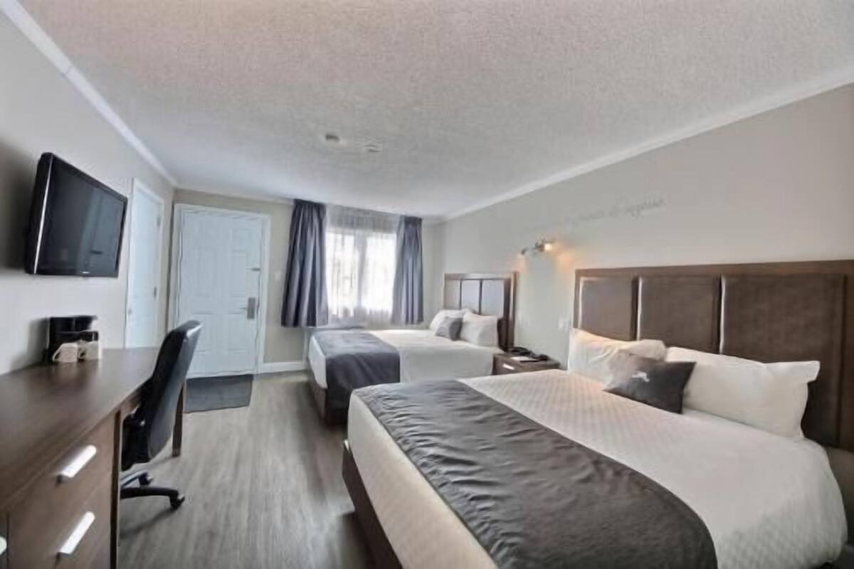 Ein Hotelzimmer mit zwei Betten, einem Schreibtisch, einem Stuhl, einem Fernseher und einer Tür.