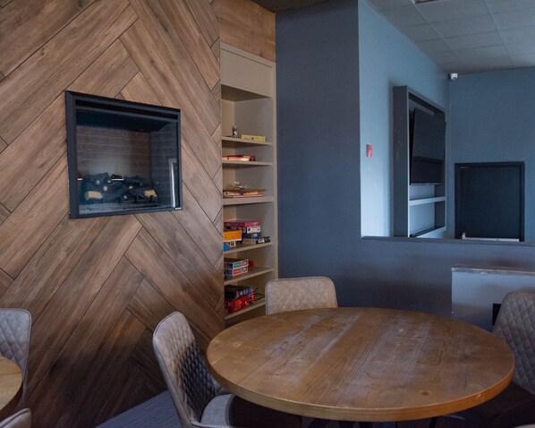 Una sala de reuniones moderna con una pared de madera en patrón de espiga, una mesa redonda de madera y una estantería empotrada con diversos objetos.