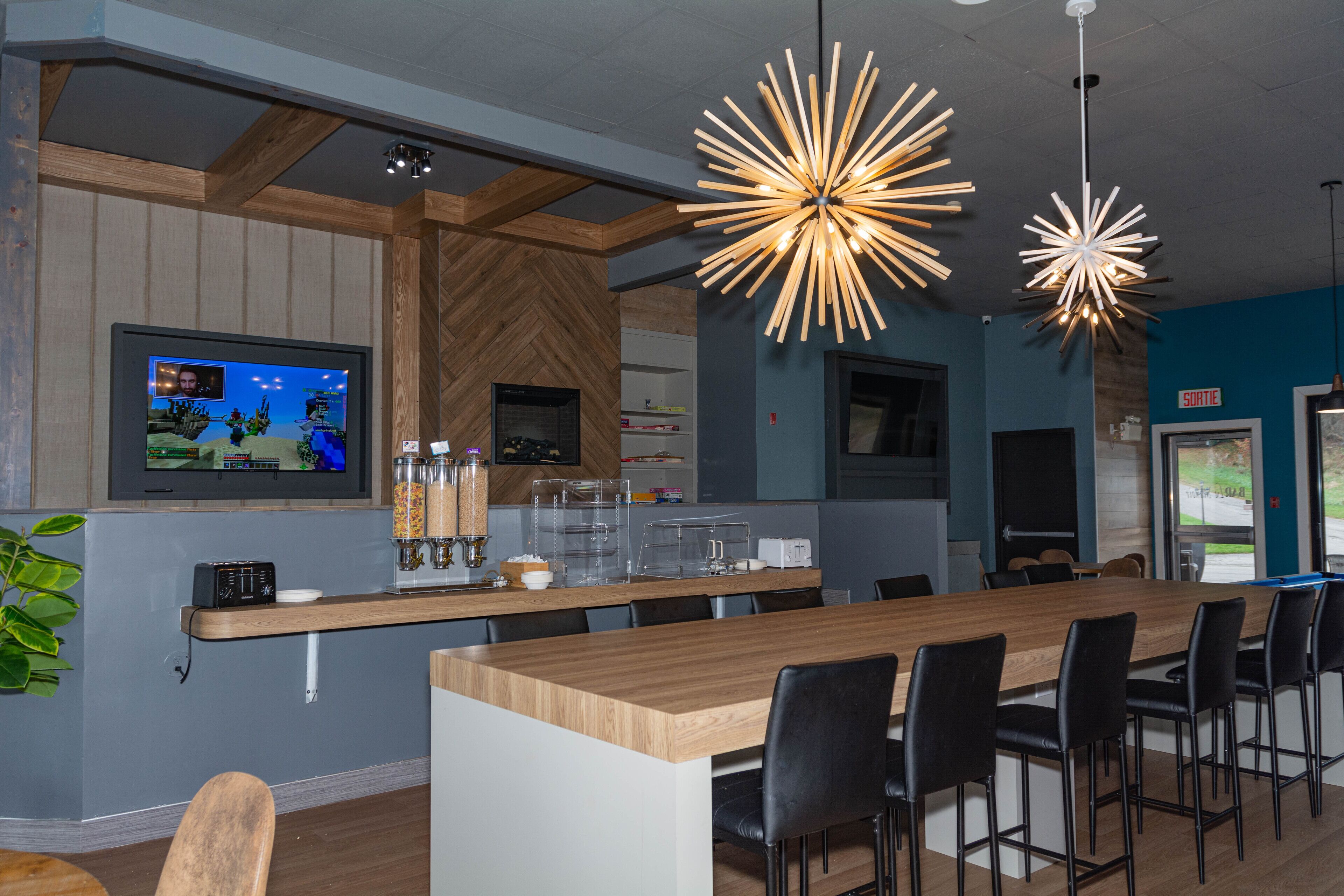 A modern bar area with a long wooden counter, black bar stools, and pendant lighting.