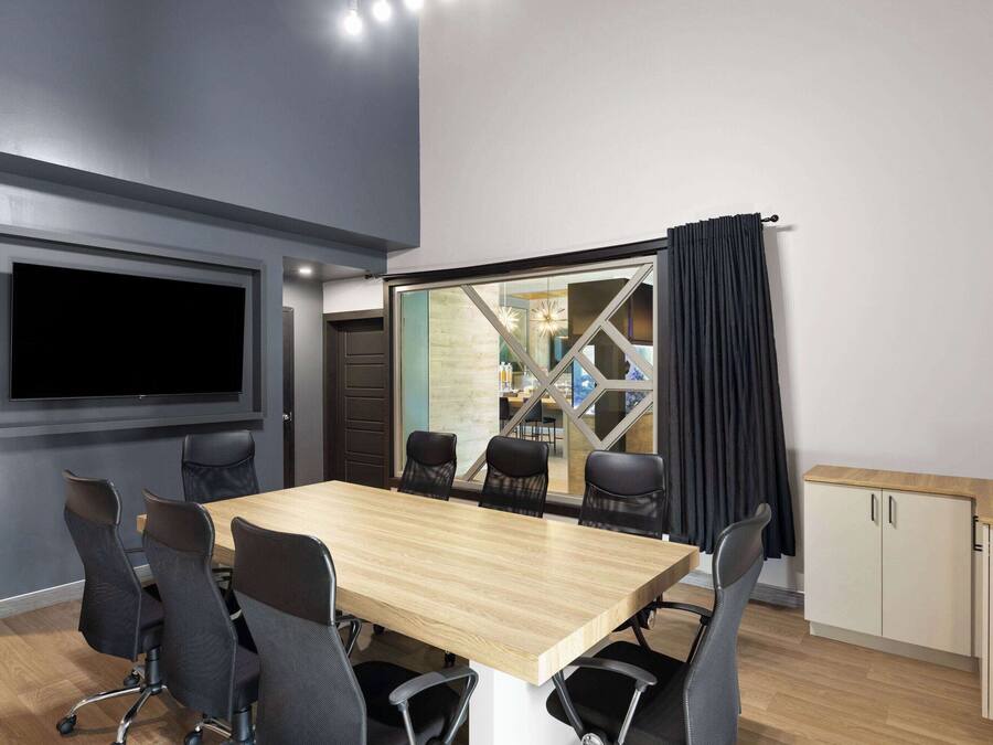 A conference room with a large table, six chairs, a flat-screen TV, and a glass partition with a view of a kitchen area.