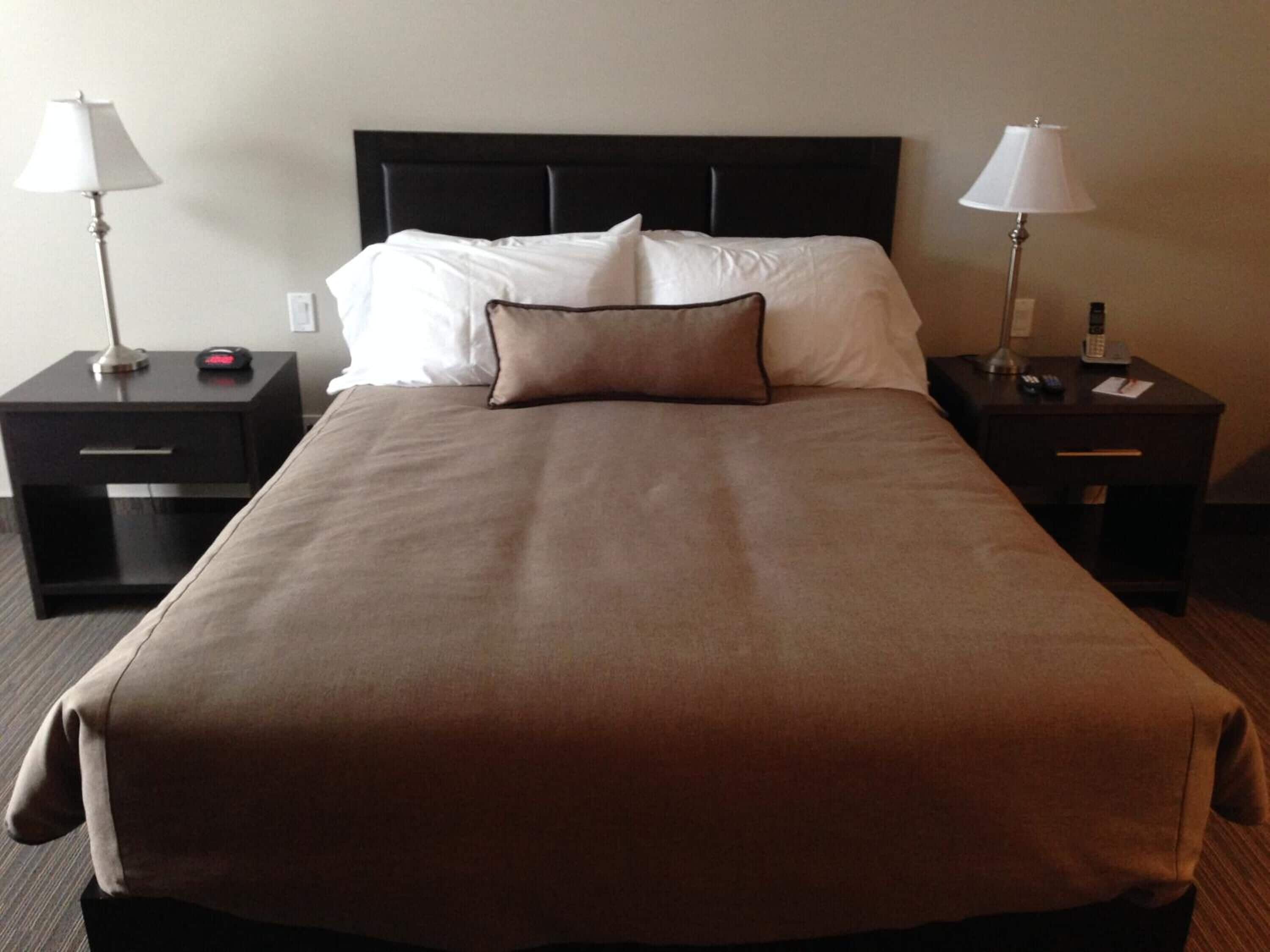 A hotel room with a large bed, two bedside tables, a black headboard, white bedding, and two bedside lamps.