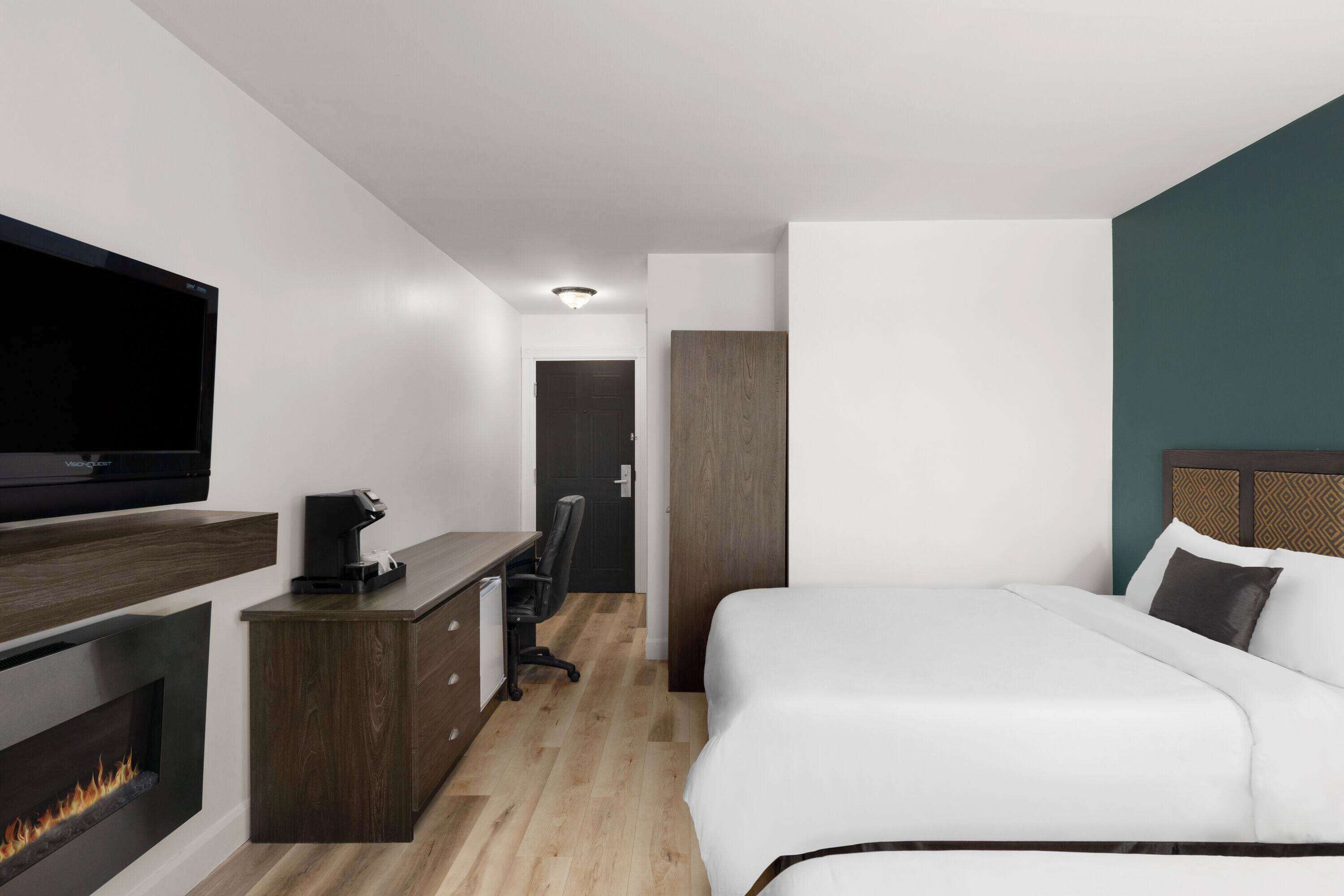 Una habitación de hotel moderna con una cama, un televisor, un escritorio con una cafetera y una chimenea.