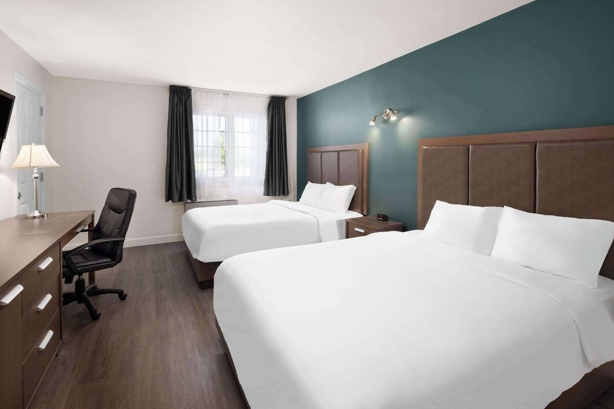 A hotel room with two beds, a desk, a chair, a lamp, and a window with curtains.