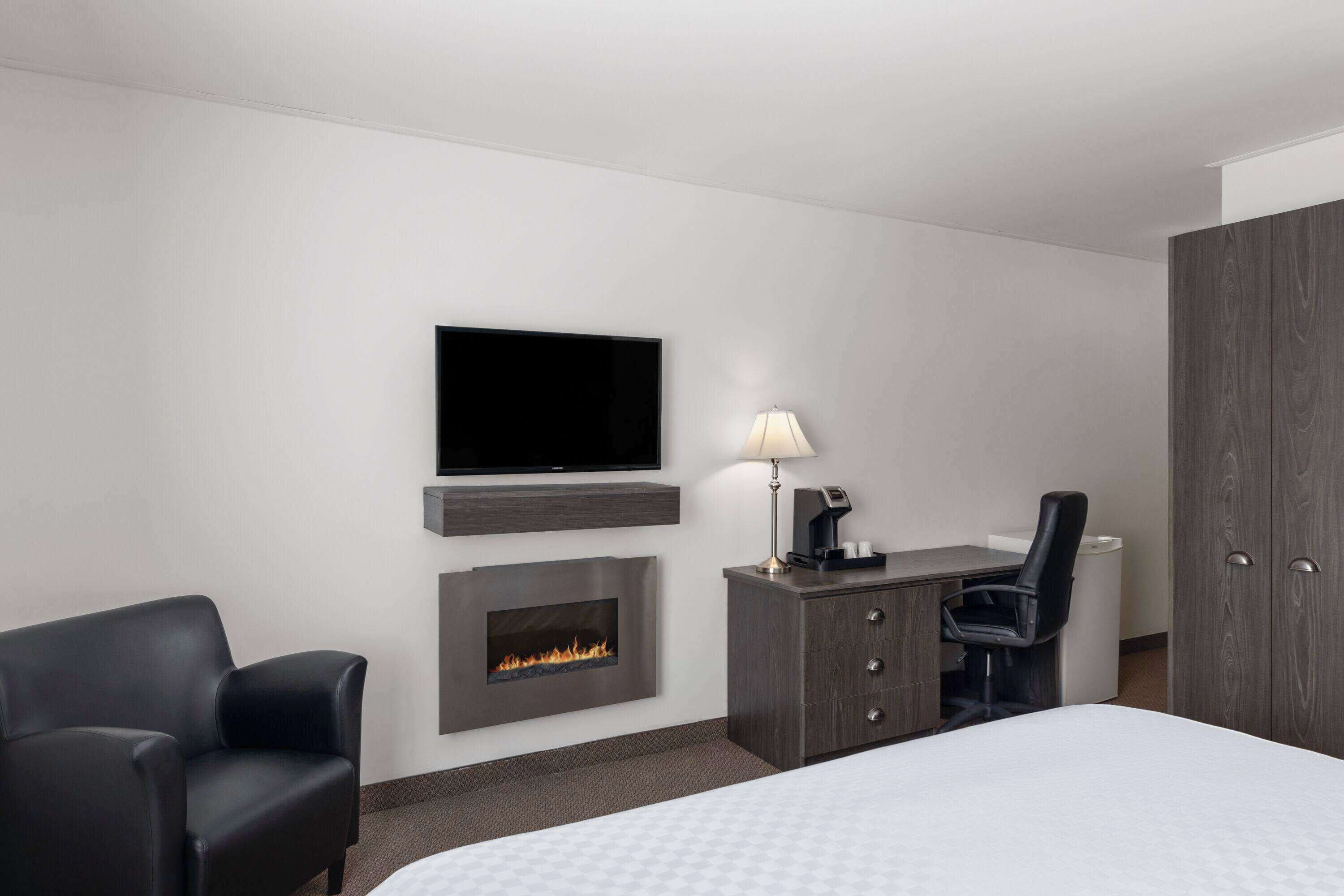 Habitación de hotel con una cama, un televisor de pantalla plana montado en la pared, chimenea, escritorio con silla y armario.