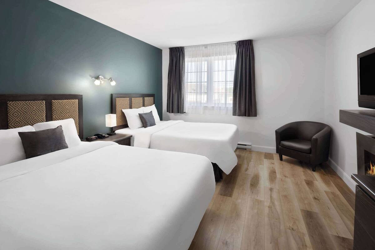 A hotel room with two beds, a TV, a chair, and a fireplace.