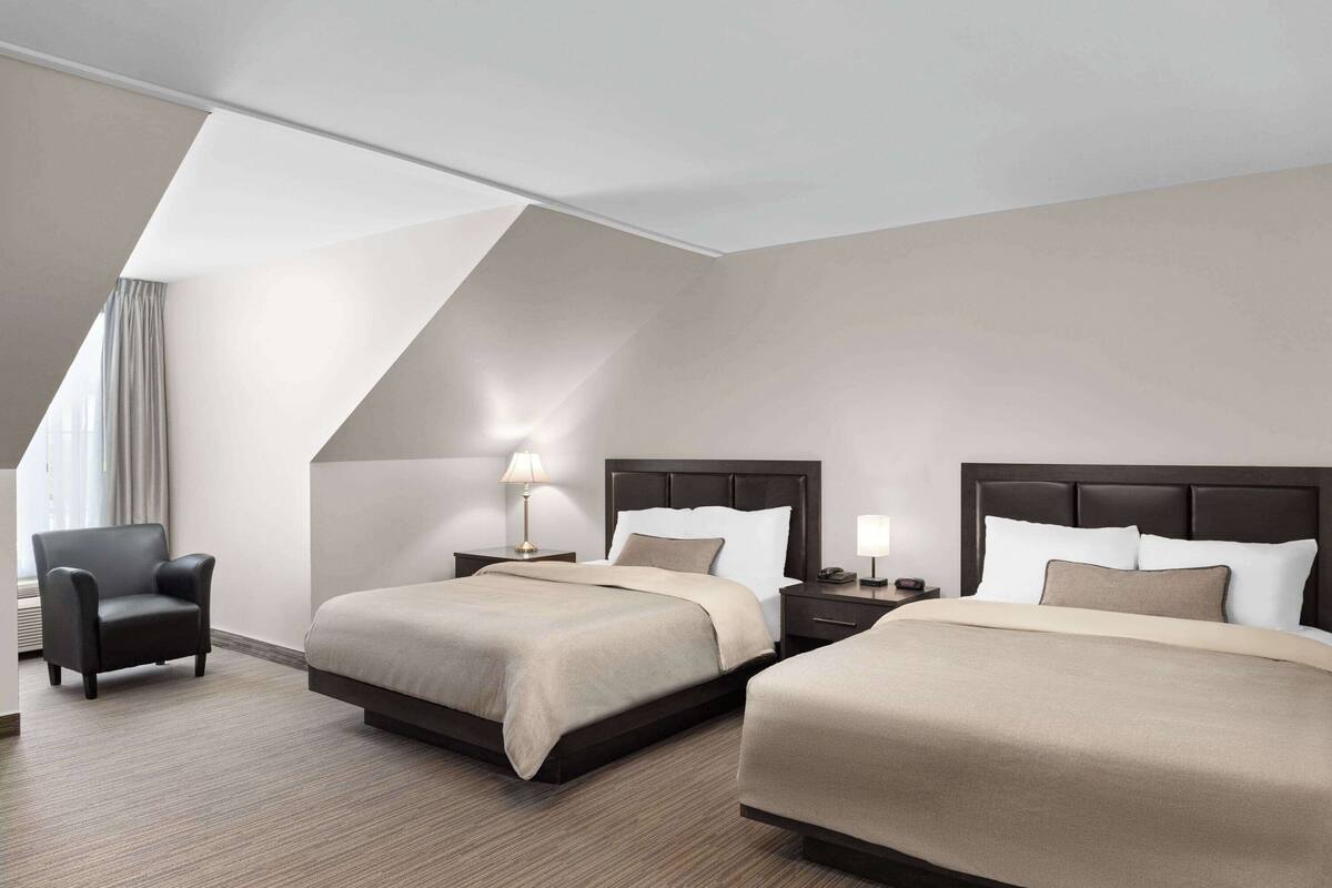 A hotel room with two beds, a chair, and a lamp.