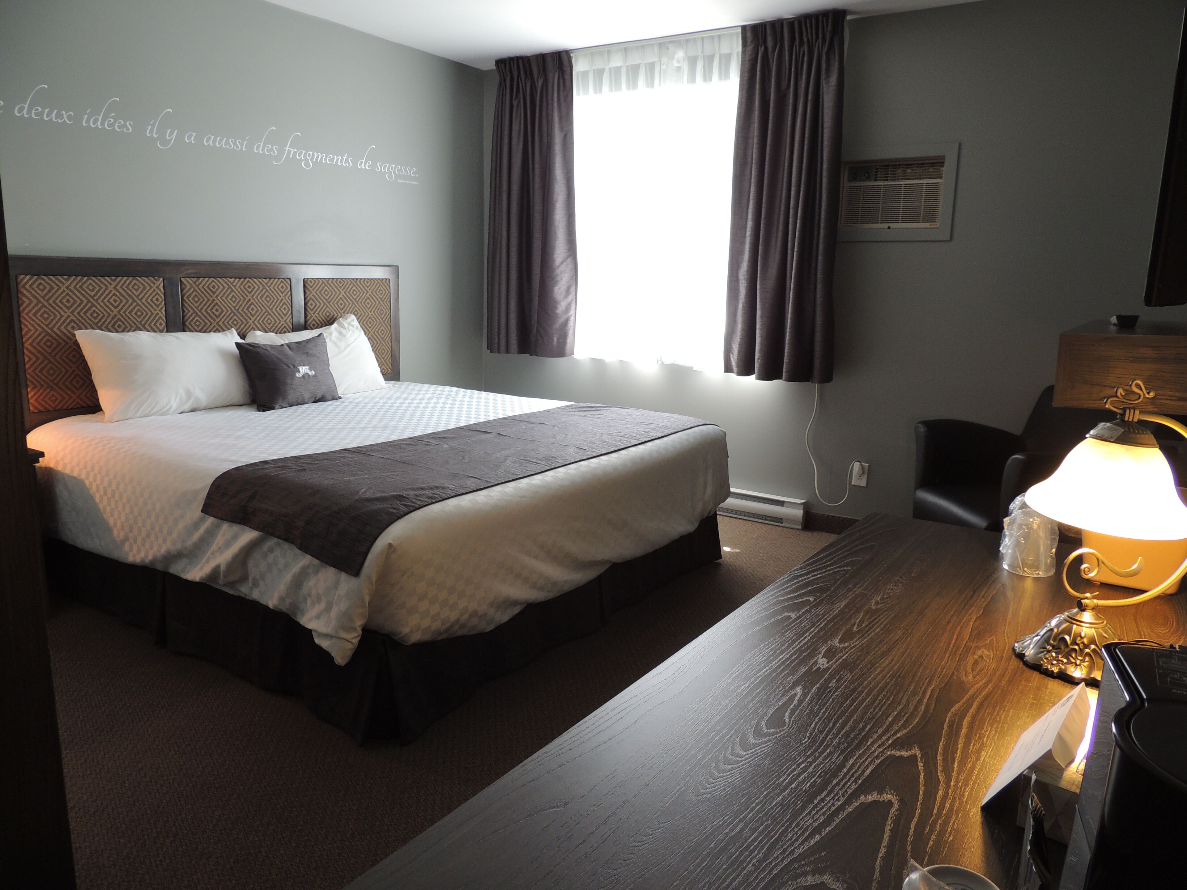 Ein Hotelzimmer mit einem großen Bett, einem Schreibtisch mit Lampe und einem Fenster mit Vorhängen.