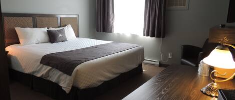 A hotel room with a large bed, a desk with a lamp, and a window with curtains.