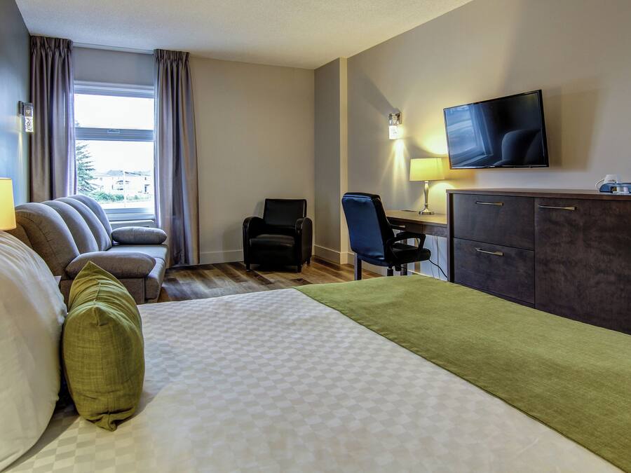Ein Hotelzimmer mit Bett, Sofa, Schreibtisch mit Stuhl, Fernseher und einer Kaffeemaschine.
