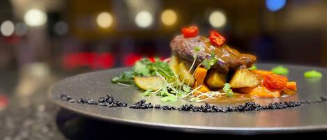 Een bord eten met een steak, groenten en garnering op een donker bord.