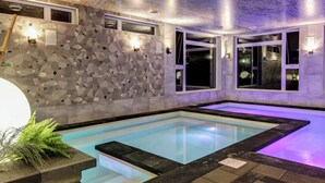 Une piscine intérieure moderne, dotée de carreaux muraux aux motifs géométriques, d’un éclairage intégré et d’un espace de baignade dégagé.