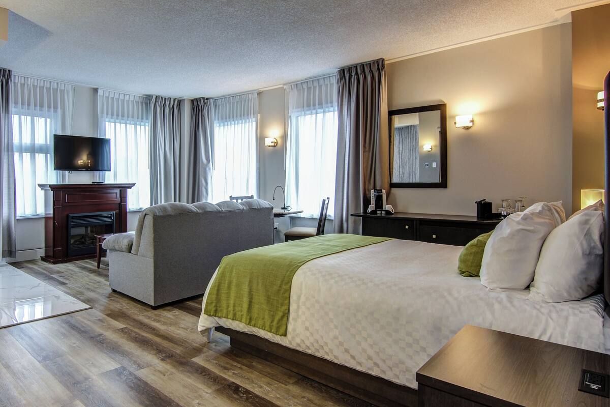 A hotel room with a bed, a sofa, a TV, a fireplace, and a desk with a lamp.