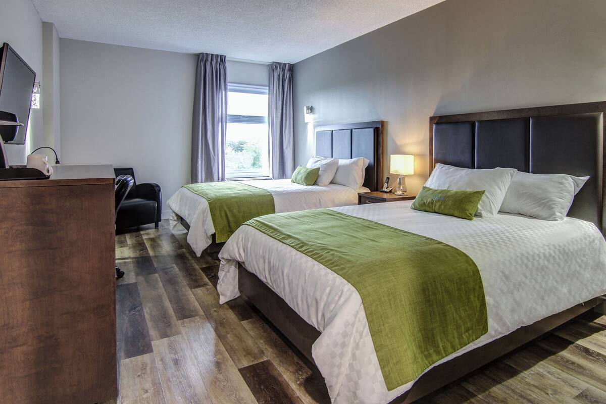 A hotel room with two beds, a desk, a chair, a lamp, and a window with curtains.