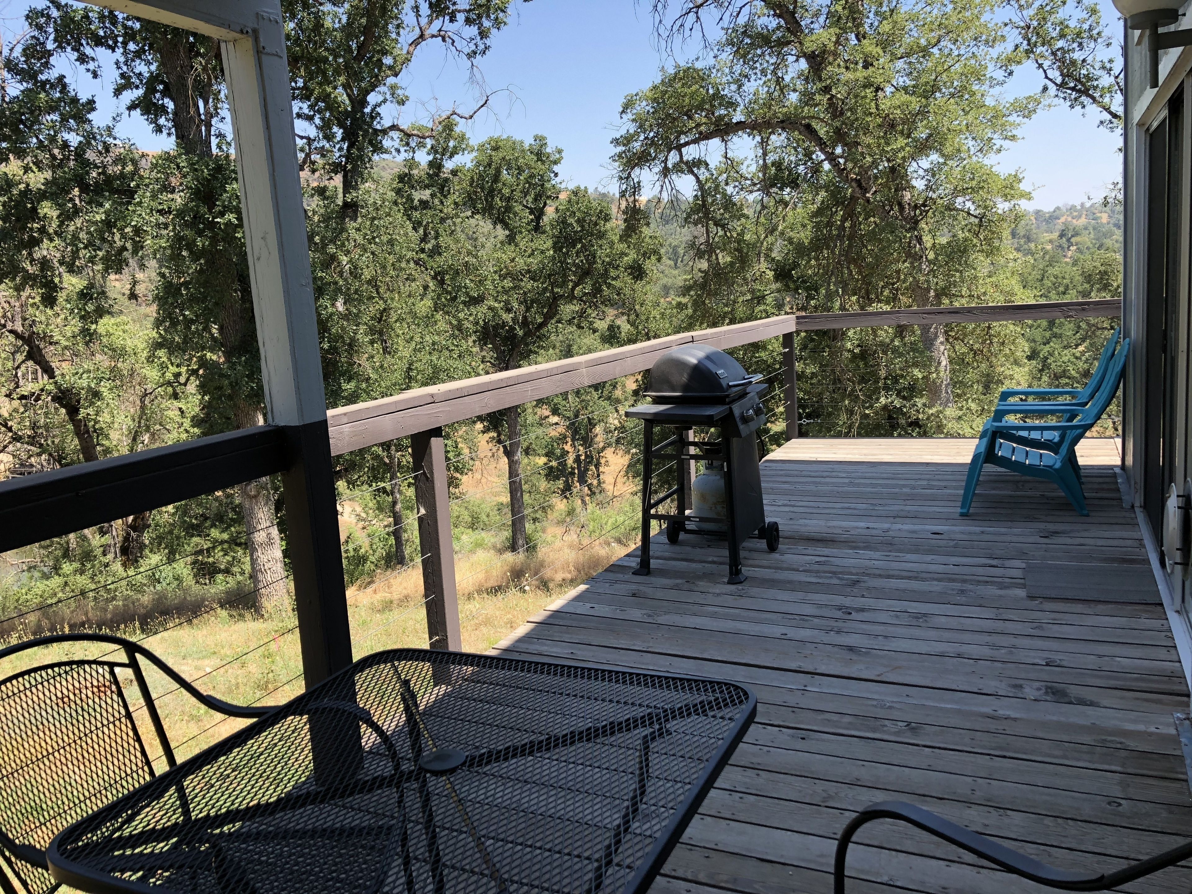 A wooden deck with a barbecue grill, a metal table, and a blue chair.