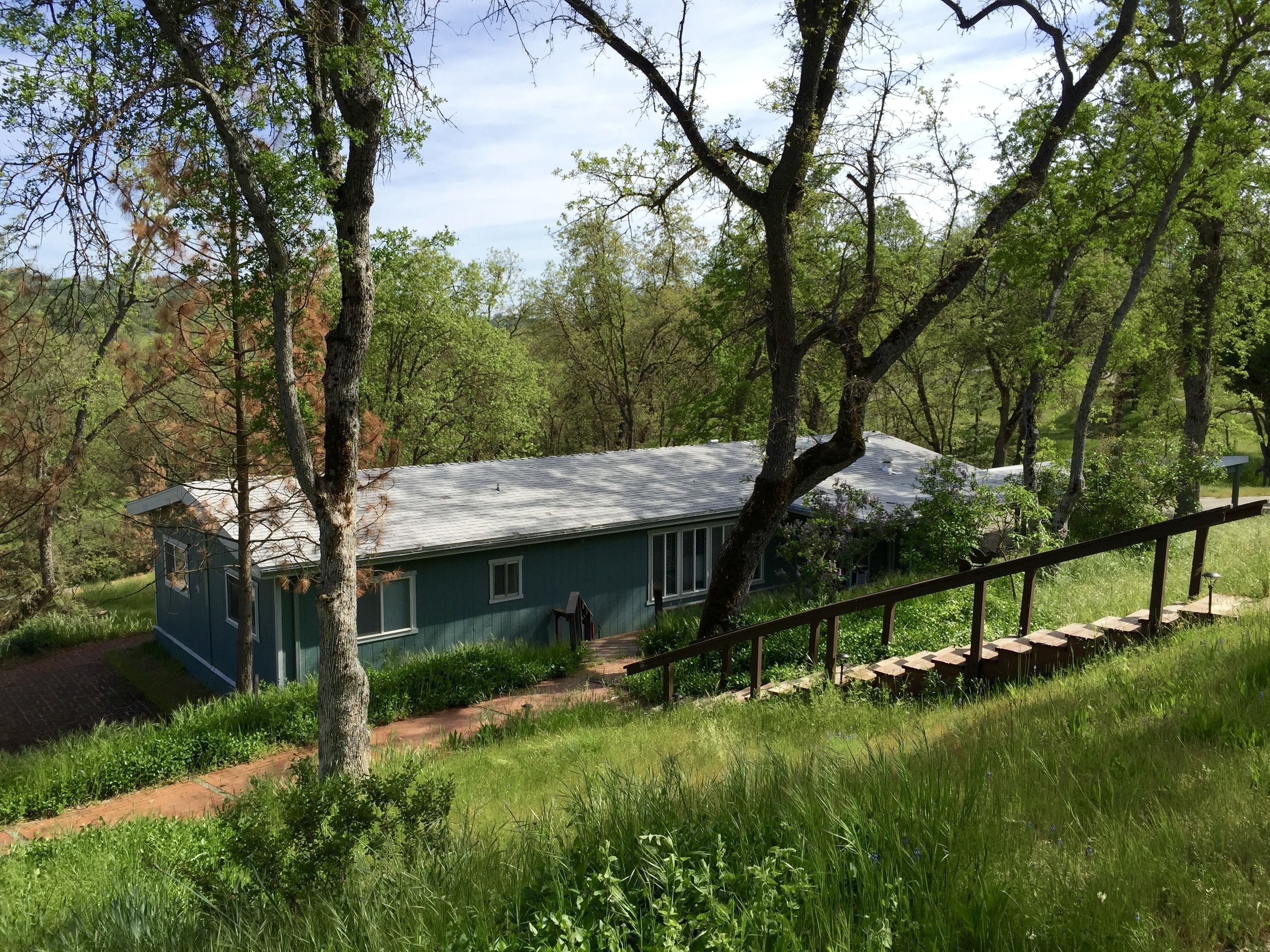 A rustic house with a sloped roof, surrounded by lush greenery and trees.
