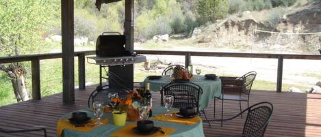 An outdoor dining area with a covered deck, a grill, and a table set for two with chairs.