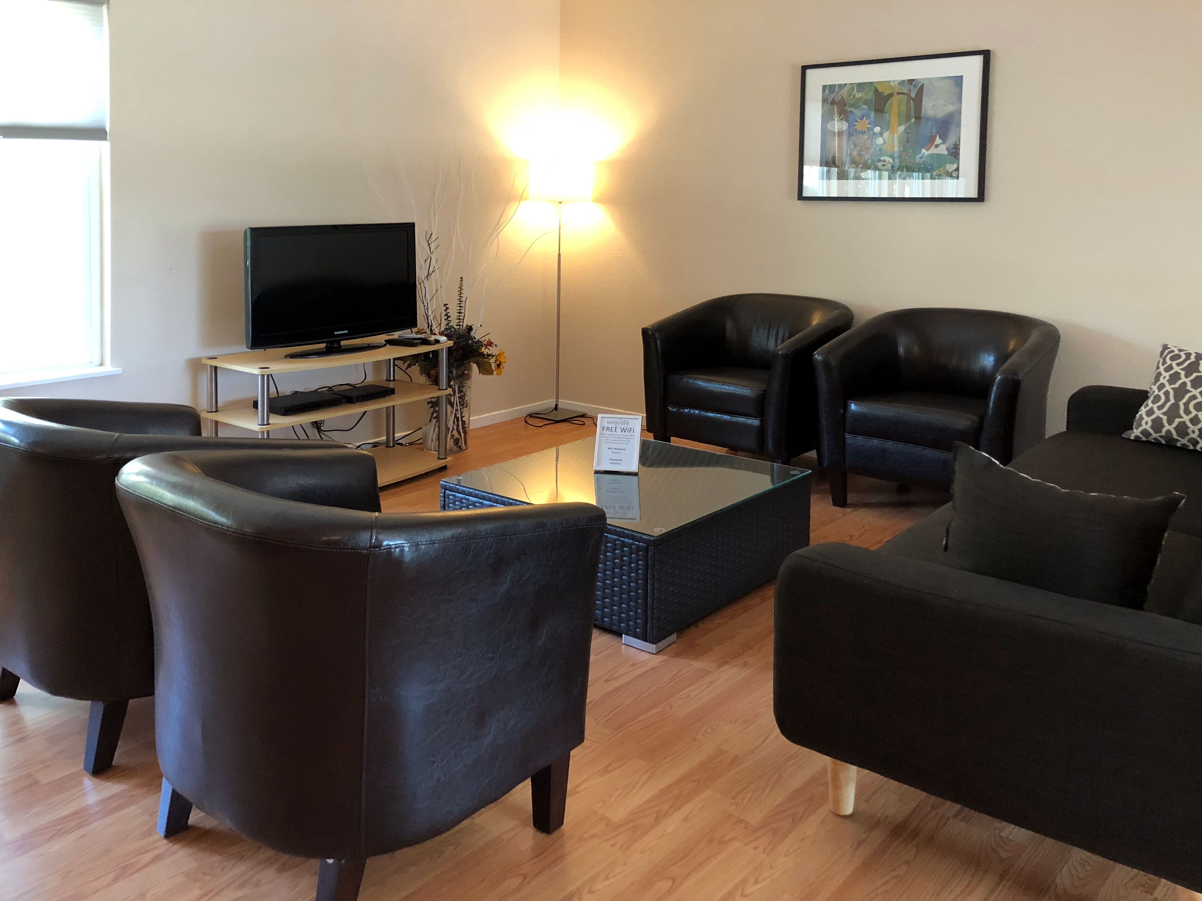 A modern living room with leather sofas, a flat-screen TV, a coffee table, and a floor lamp.