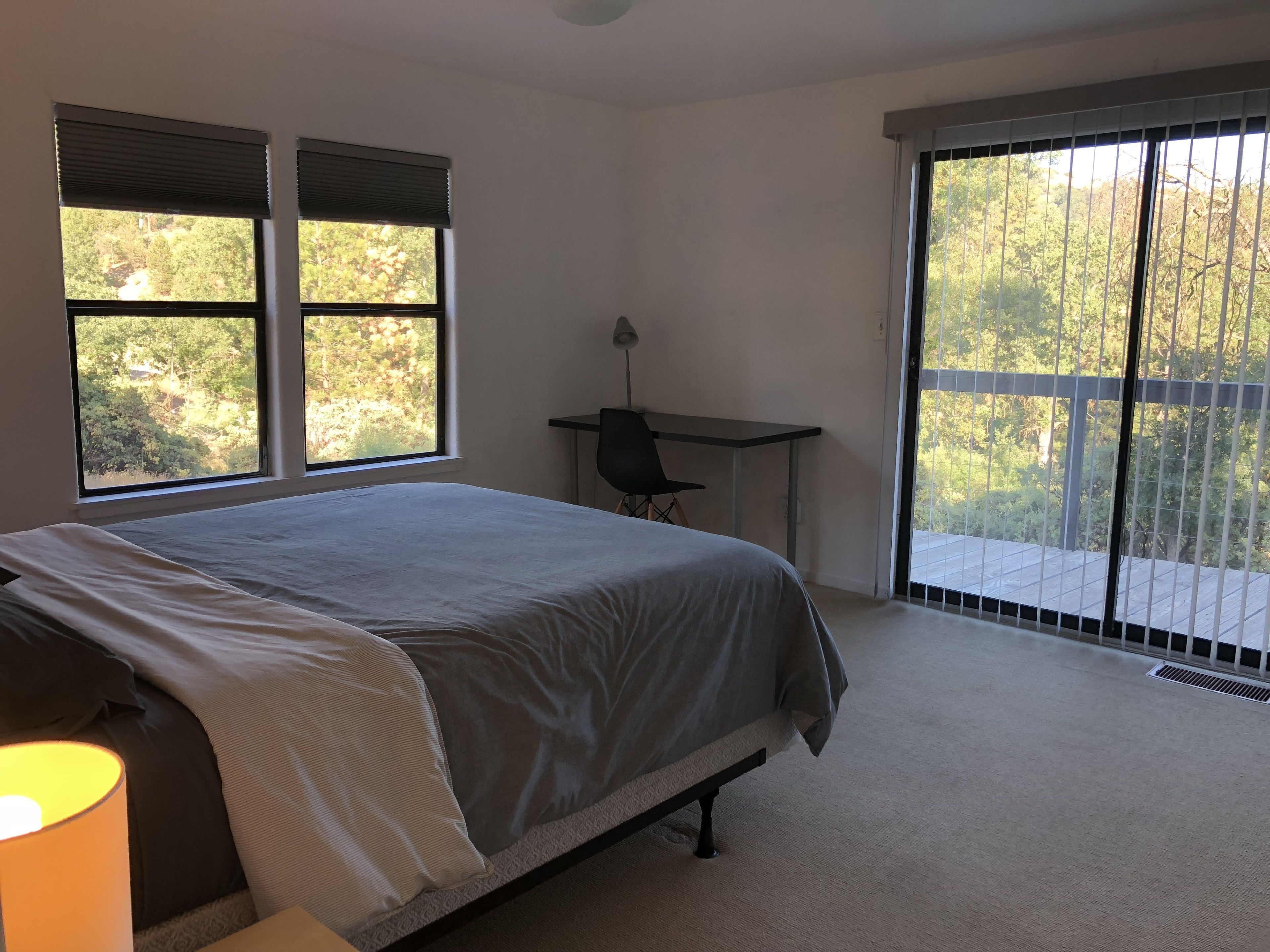 Un dormitorio con cama, escritorio y vista a árboles por las ventanas.