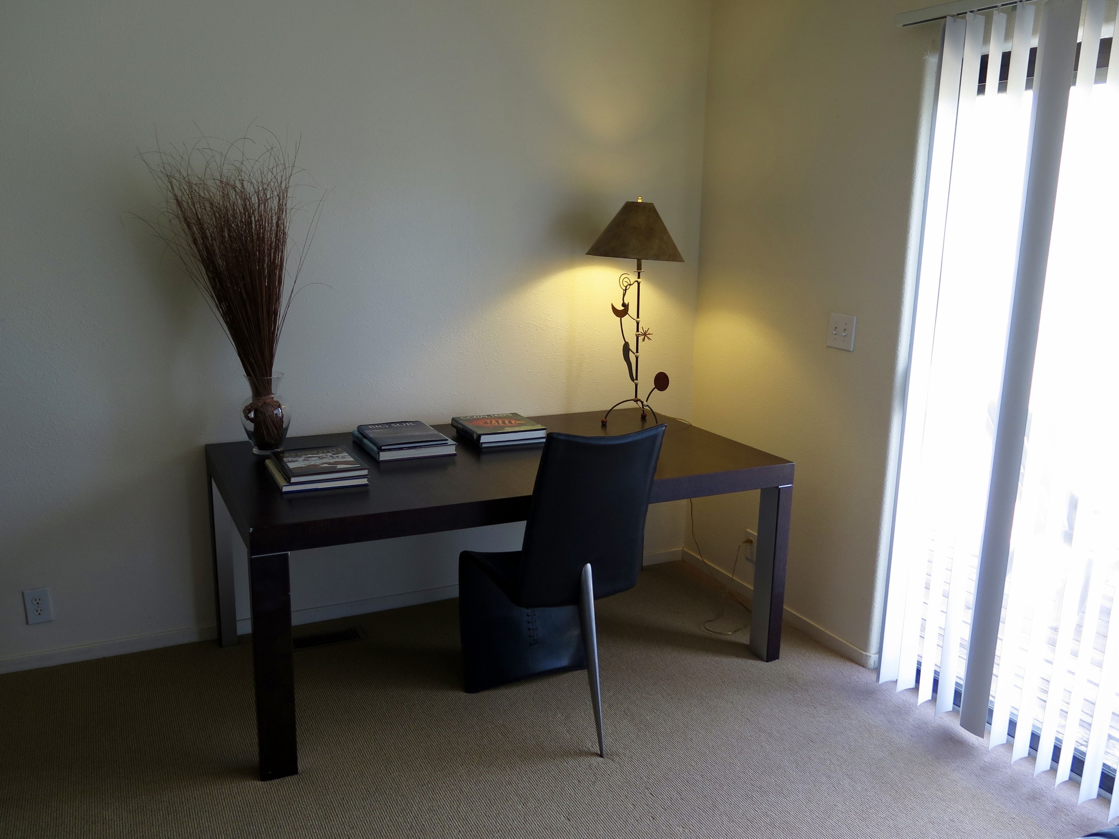 Quarto com escrivaninha, cadeira, abajur e livros.