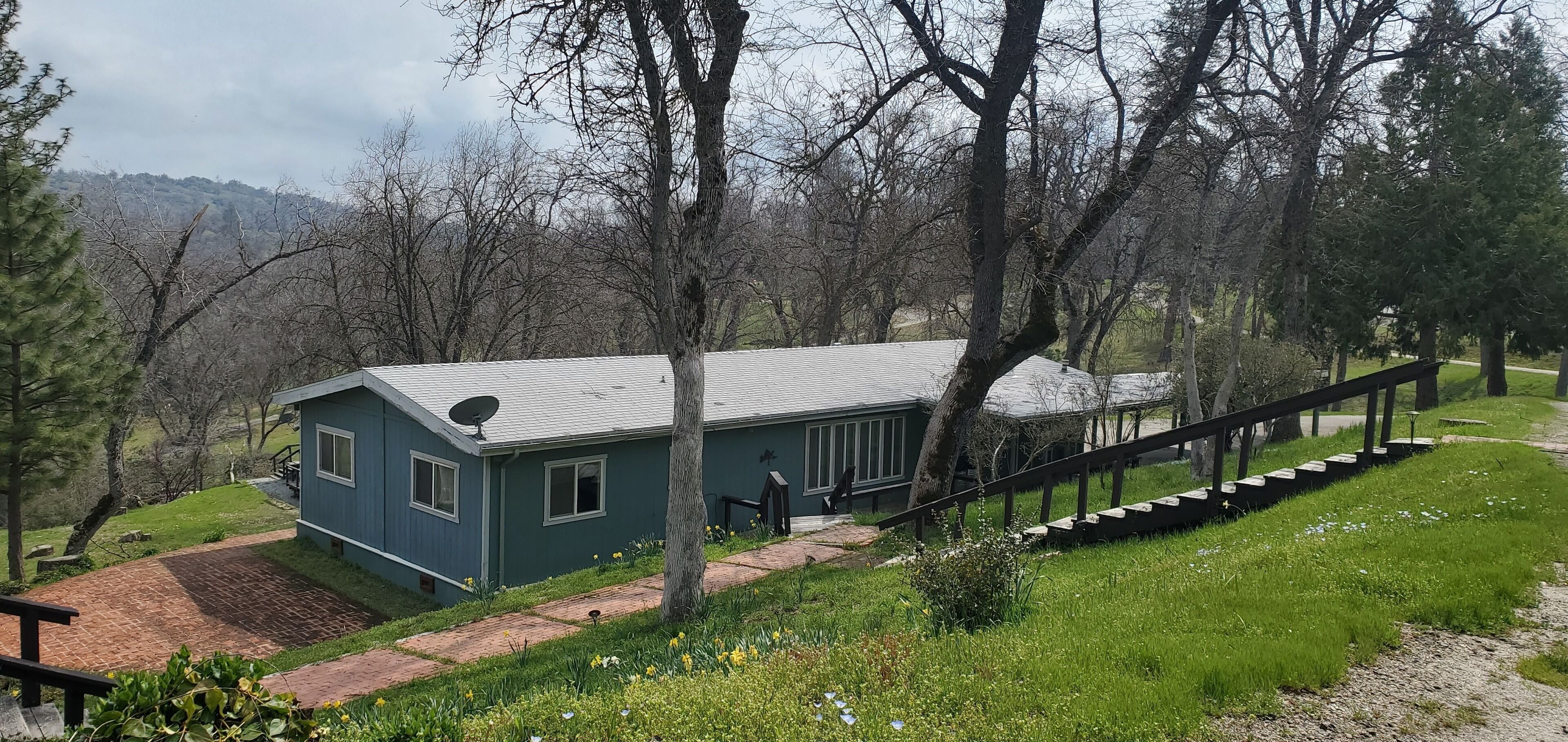 A blue house with a satellite dish, a covered porch, and a staircase leading to a deck.