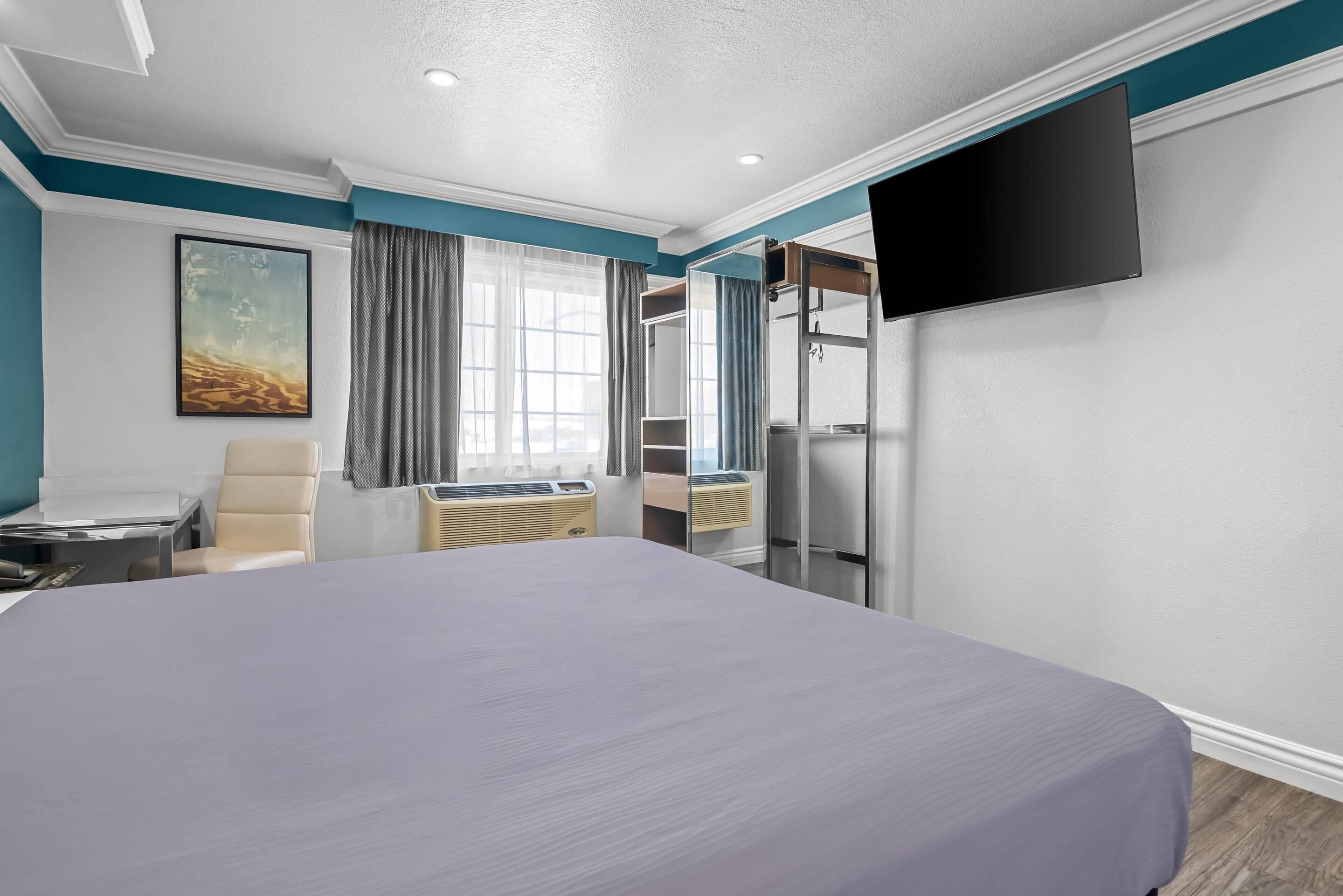 A hotel room with a bed, a desk, a chair, a TV, and a window with curtains.