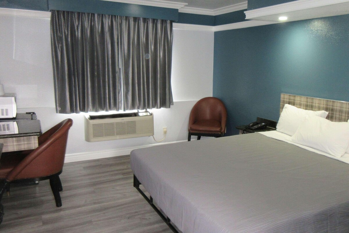 A hotel room with a bed, a desk with a computer, a chair, a telephone, and a window with curtains.