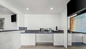 A modern kitchen with white cabinetry, a black countertop, and a flat-screen TV mounted on the wall. - Rodeway Inn Commerce - Los Angeles (Los Angeles)