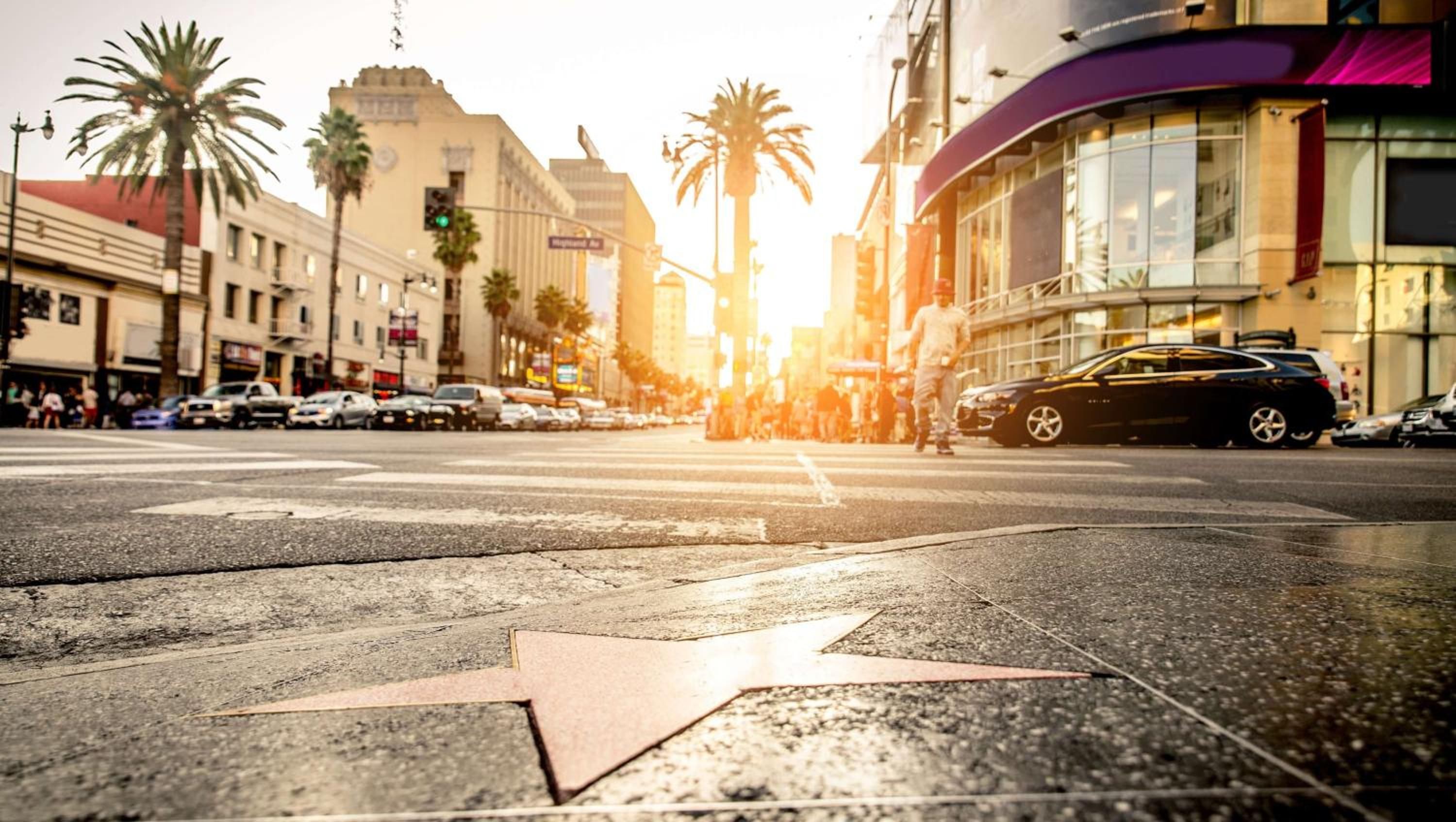 A street intersection with a star-shaped pedestrian crossing, palm trees, and buildings with commercial signage.