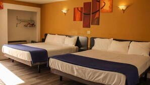 A hotel room with two beds, each with a blue bedspread and white pillows. There are wall-mounted light fixtures and a painting on the wall. - Motel 6 Glendale, CA – Pasadena Burbank Los Angeles (Glendale)