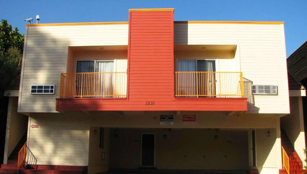 Un edificio a due piani con una sezione centrale rossa e pareti beige, dotato di un balcone al piano superiore.