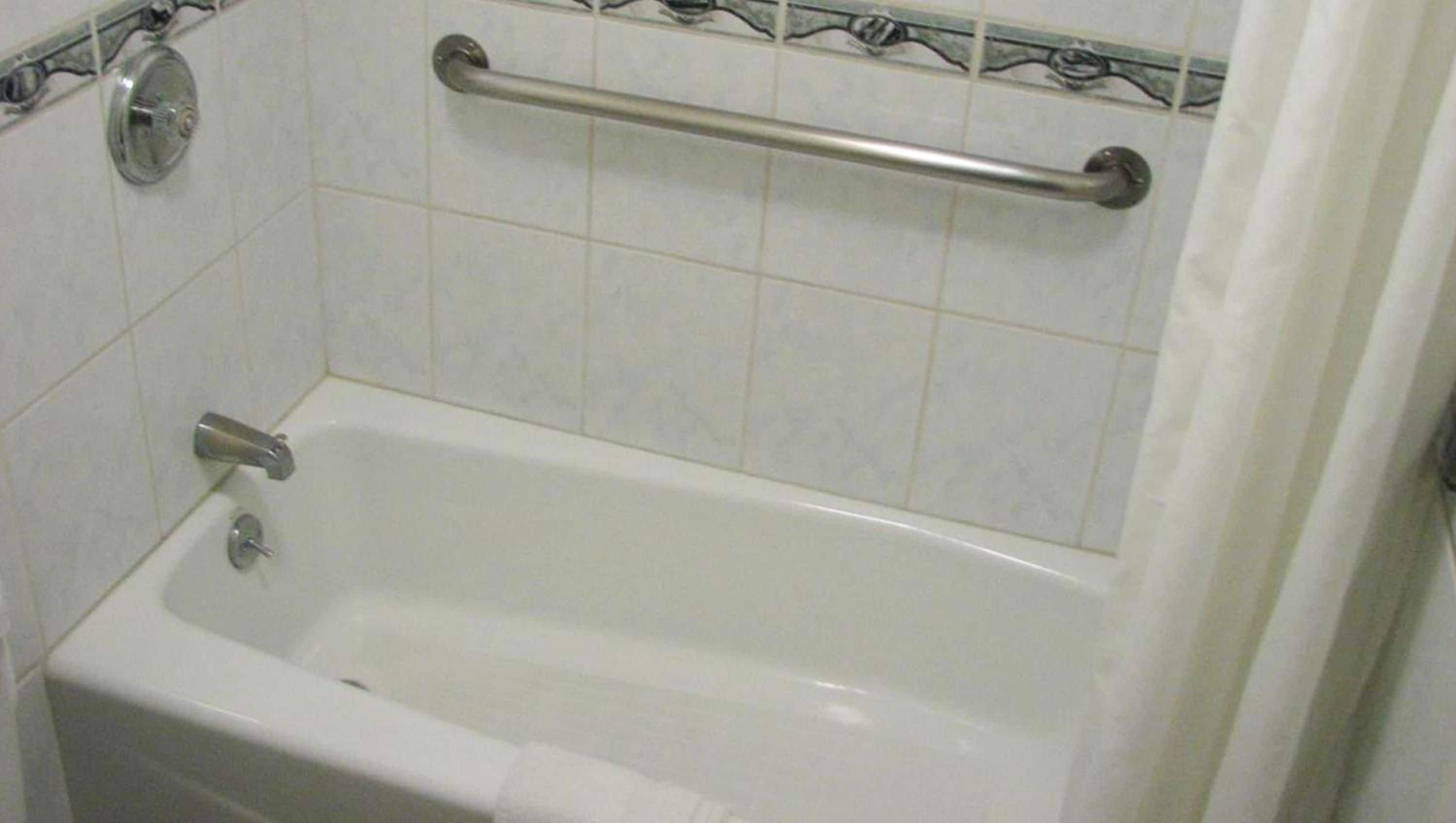 Una bañera estándar con una barra de apoyo, un grifo y un cabezal de ducha.