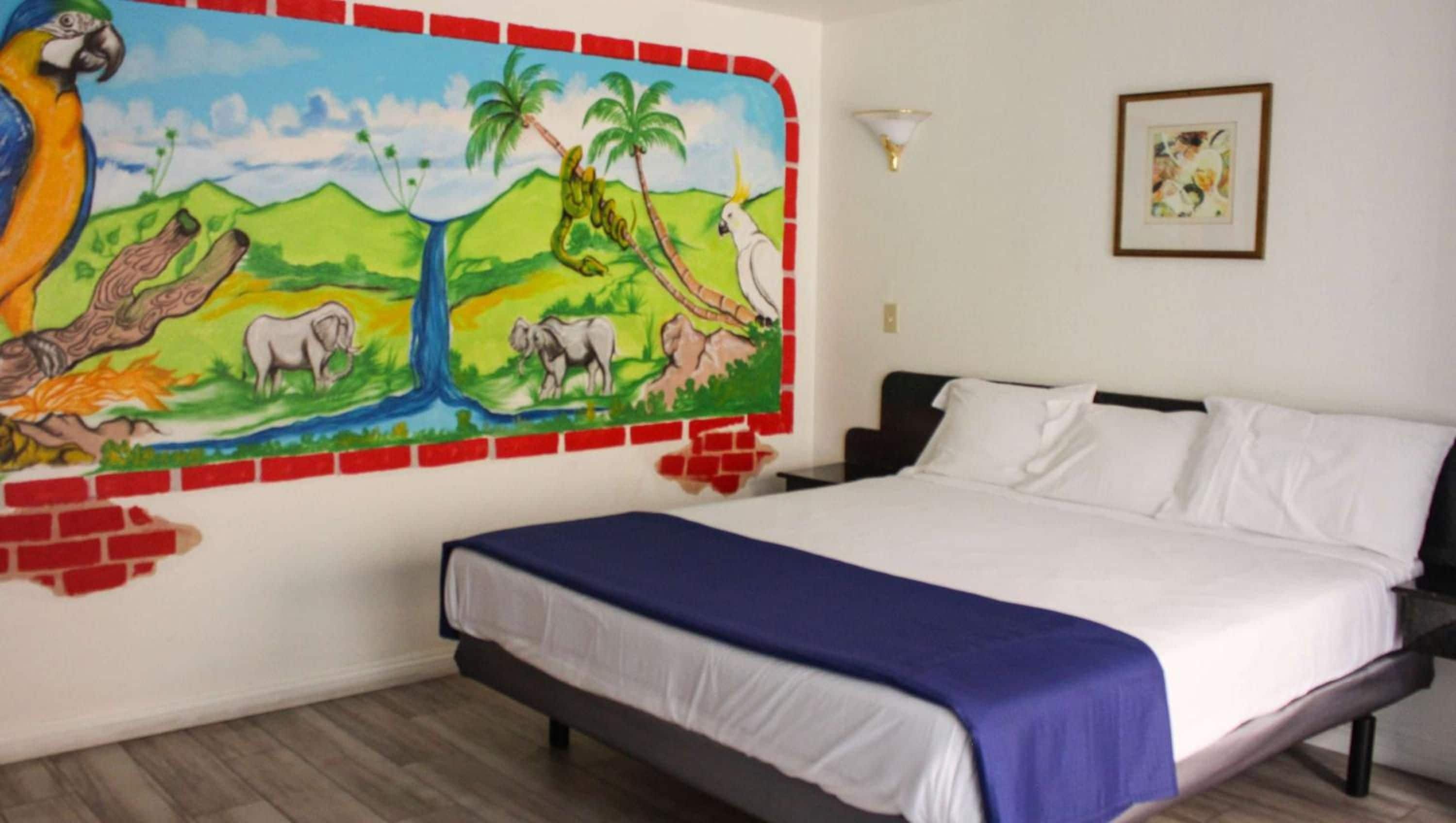 A bedroom with a bed, a mural on the wall, and a framed picture.